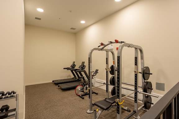 A gym with a variety of equipment including a treadmill, weight rack, and bench.
