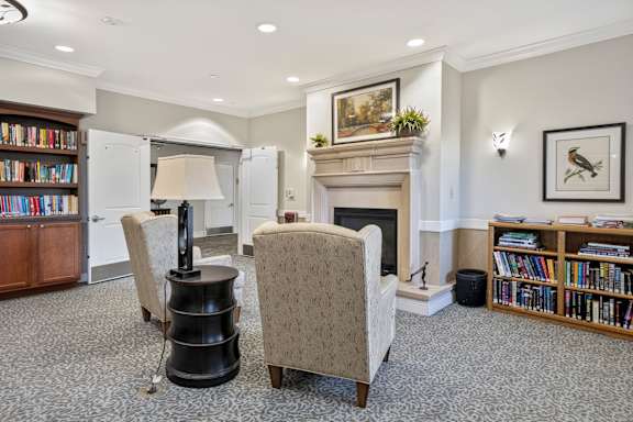 Library reading nook room with a fireplace, two chairs, and a bookshelf at Lakeview Senior Living Apartments, Lakewood