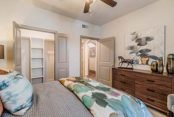 A bedroom with a bed, dresser, and ceiling fan. at Atlas Point at Prestonwood Apartments , Texas, 75010