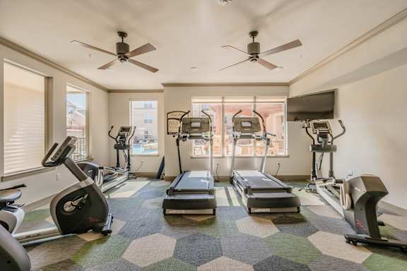 A spacious gym with treadmills, elliptical machines, and a fan. at Atlas Point at Prestonwood Apartments , Texas, 75010