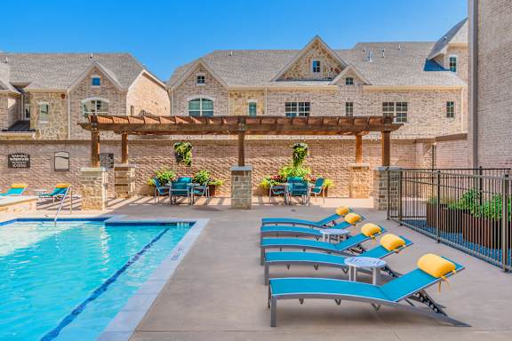 A pool with sun loungers and a building in the background. at Atlas Point at Prestonwood Apartments , Carrollton, TX