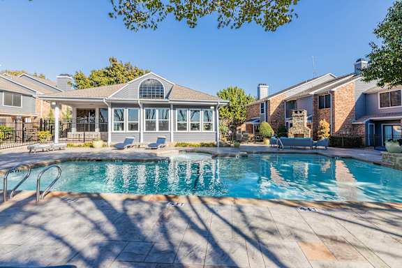 A swimming pool in a backyard with a house and a gazebo in the background. at Avalon Villas Apartments , Irving, Texas