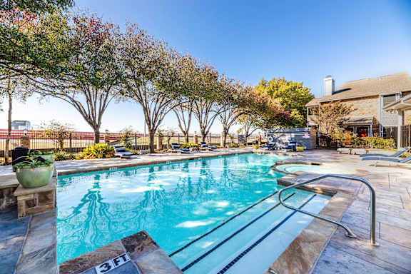A swimming pool surrounded by trees and a building in the background. at Avalon Villas Apartments , Irving, TX
