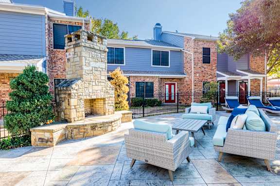 A patio with a stone fireplace and wicker furniture. at Avalon Villas Apartments , Texas