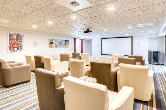 A conference room with a white screen and beige chairs. at King City Senior Village Apartments, King City, OR, 97224