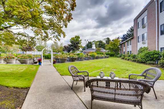 A patio with a bench and chairs is surrounded by a grassy area and apartment buildings. at King City Senior Village Apartments, King City, OR