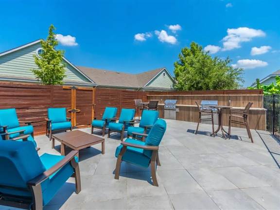 A patio with blue chairs and a table is set up. at Sunstone Village Apartments, Denton, TX, 76208