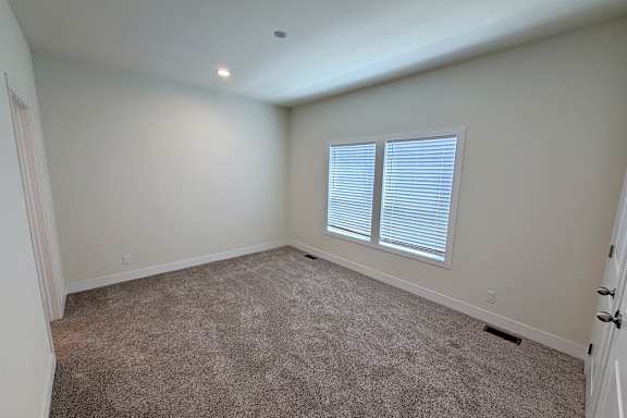 A room with carpeted floor and a window with blinds.