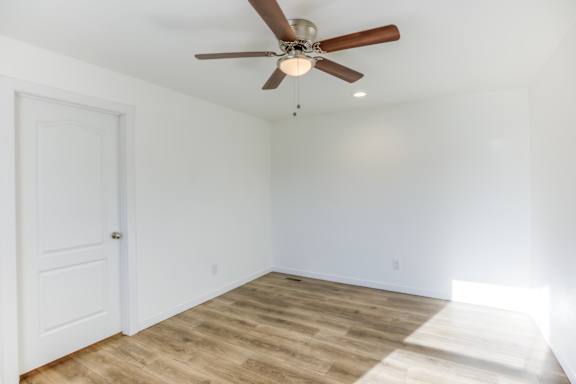 A room with a ceiling fan and wooden flooring.