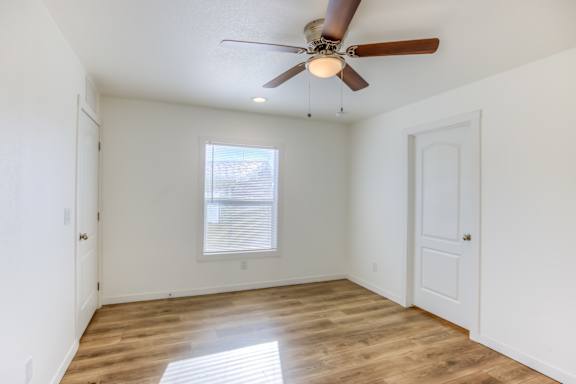 A room with a ceiling fan and wooden flooring.
