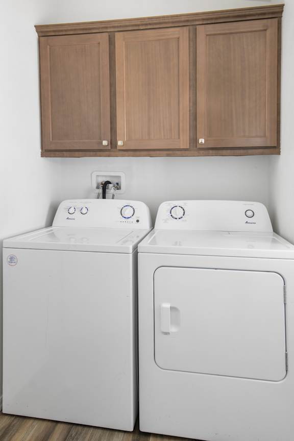 Two white washing machines in front of brown cabinets.