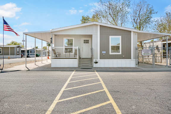 A small building with a flag on the left side and a parking lot in front.