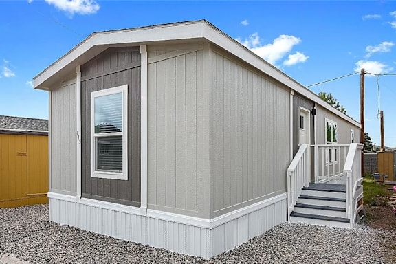 A small house with a grey siding and a brown door.