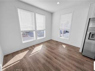 A sunny room with a wooden floor and a refrigerator.