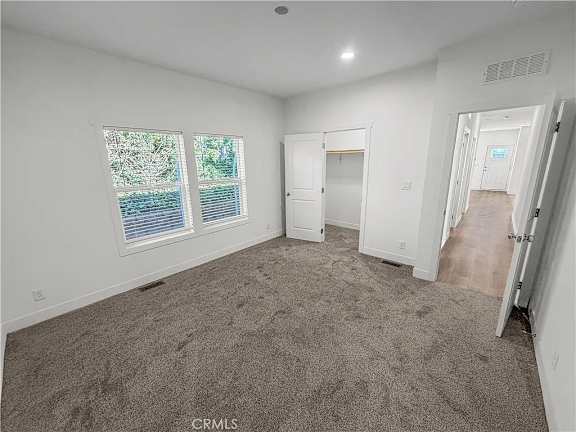 A bedroom with a carpeted floor, two windows, and a door leading to another room.