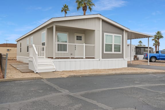 a beige manufactured home with a porch and a blue truck in front of it