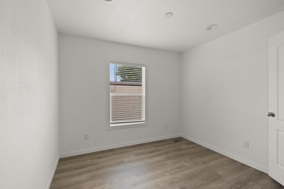 a bedroom with white walls and wood flooring and a window