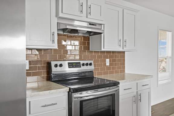 A modern kitchen with a stove top oven and white cabinets.