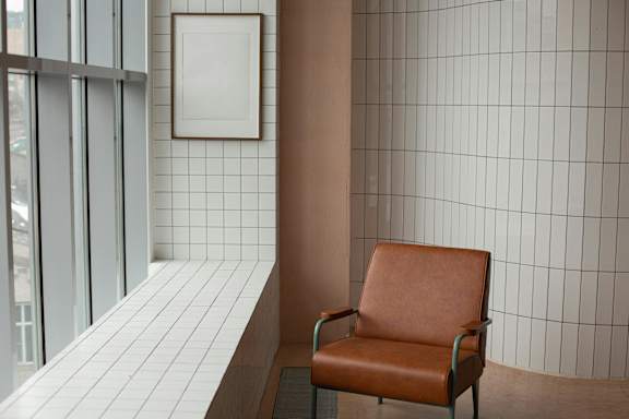 A brown leather chair sits in front of a wall with white tiles.