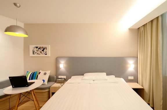 A well-lit bedroom with a large bed and a laptop on a table.