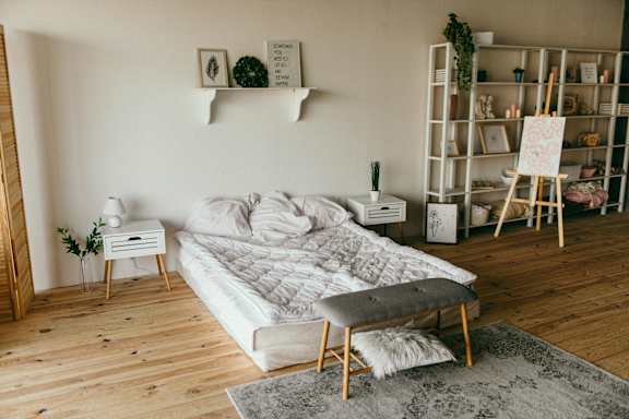 A white bed with a grey pillow and a grey cushion on it.