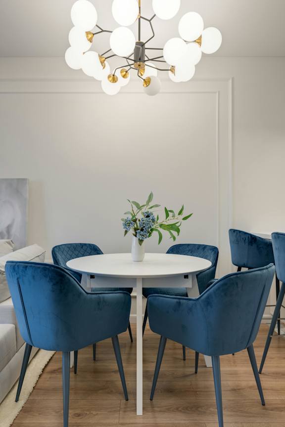 A white table with blue chairs and a chandelier with white lights.