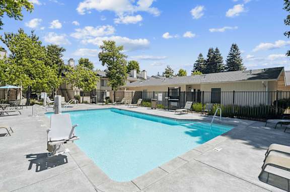 A swimming pool surrounded by lounge chairs and trees.