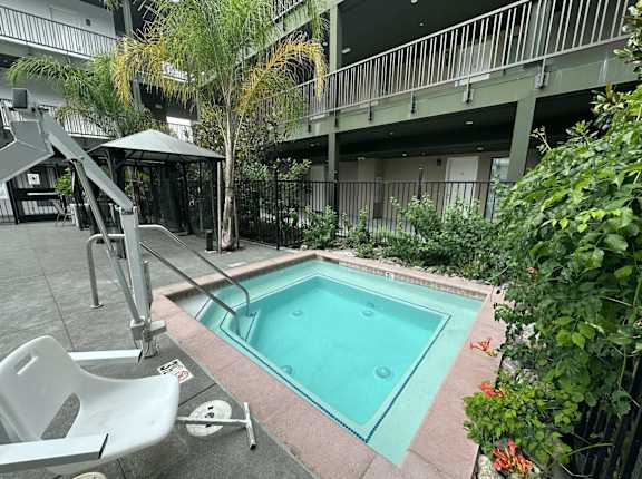 A small pool in a courtyard surrounded by plants and a chair.