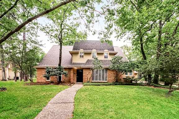 A house with a brick facade and a black door is surrounded by greenery.