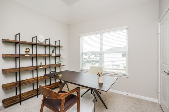 a desk and chair in a room with a window and a bookshelf