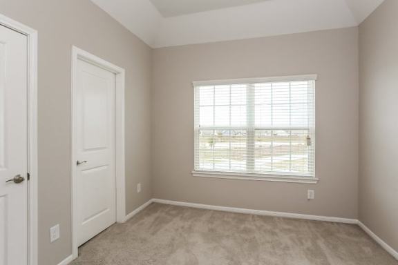 A room with a carpeted floor and a window with blinds.