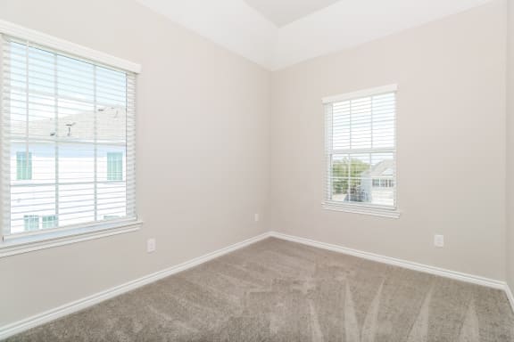 an empty bedroom with two windows and a carpeted floor