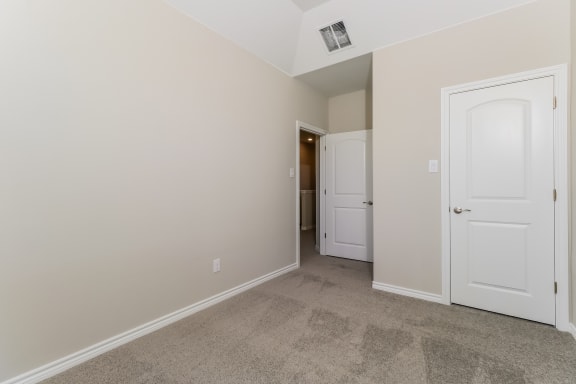 an empty bedroom with white doors and a carpeted floor