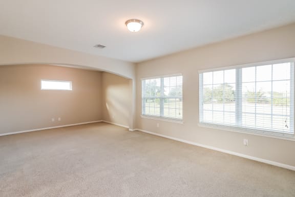 an empty living room with large windows and carpeting