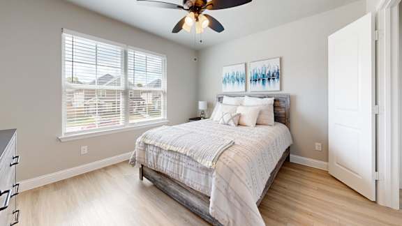 A bedroom with a bed, a ceiling fan, and a window with blinds.