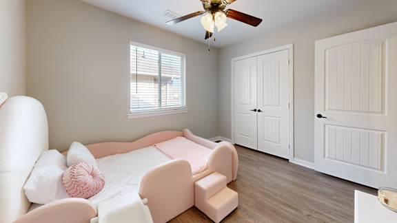 A pink bed with a white headboard and footboard sits in a room with a ceiling fan and two doors.