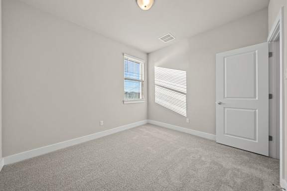 A room with a carpeted floor, a window with blinds, and a white door.