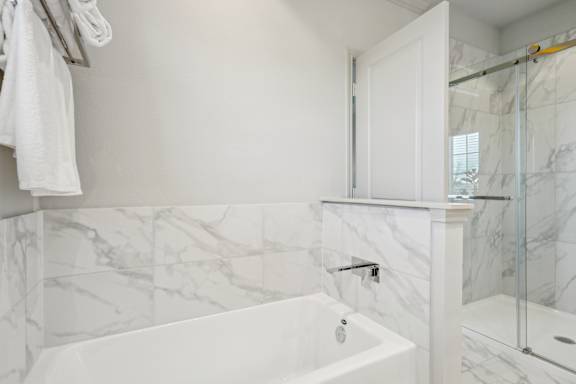 A white bathroom with a marble tile wall and a white tub.