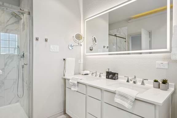 A white bathroom with a sink, mirror, and shower.