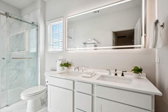 A white bathroom with a toilet, sink, and mirror.