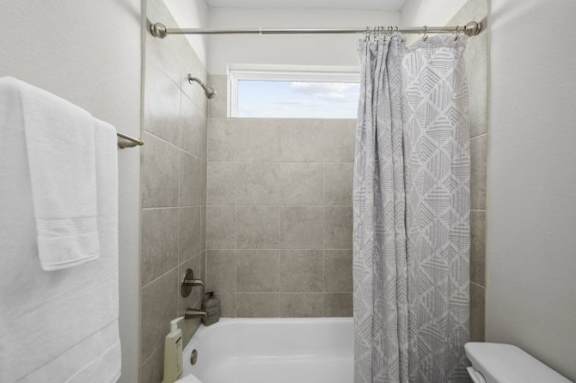 A bathroom with a white tub, grey shower curtain, and a white towel hanging on the towel rack.