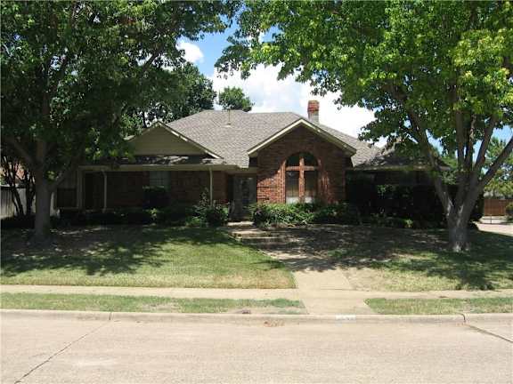 A house with a brown roof and a brick chimney is surrounded by trees.