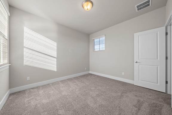 A room with a carpeted floor, a window with blinds, and a door.