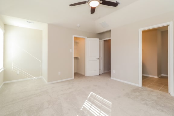 an empty living room with a ceiling fan and a door to a bathroom