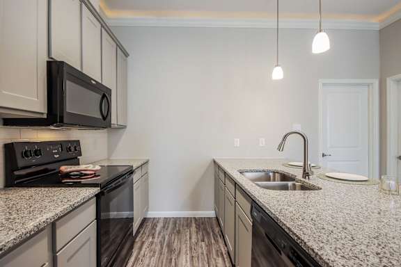 A kitchen with a black microwave above a stove and a sink with a faucet.
