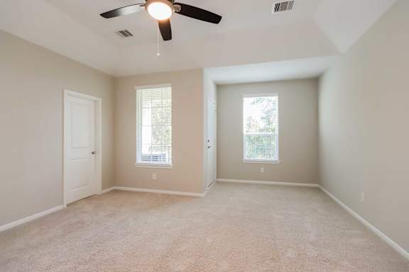 A room with a ceiling fan and two windows.