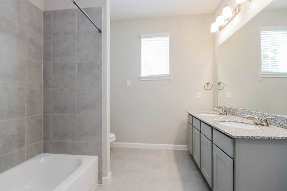 A bathroom with a white tub and grey tiles.