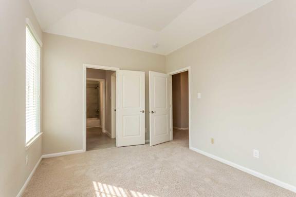 A room with a carpeted floor and white walls, with a door open to another room.