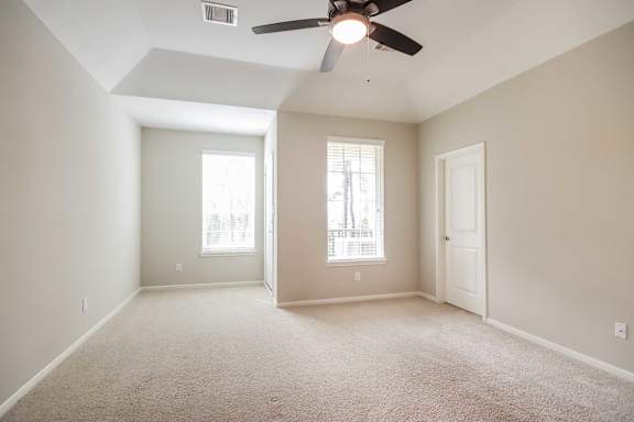 A room with a ceiling fan and two windows.