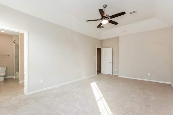 A room with a ceiling fan and a toilet visible through the door.